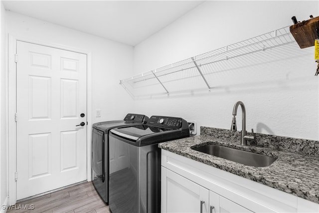 laundry room featuring cabinets, sink, washer and dryer, and light hardwood / wood-style flooring