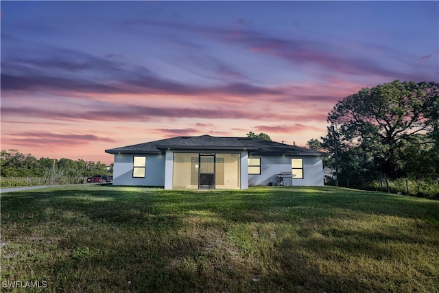 back house at dusk featuring a lawn