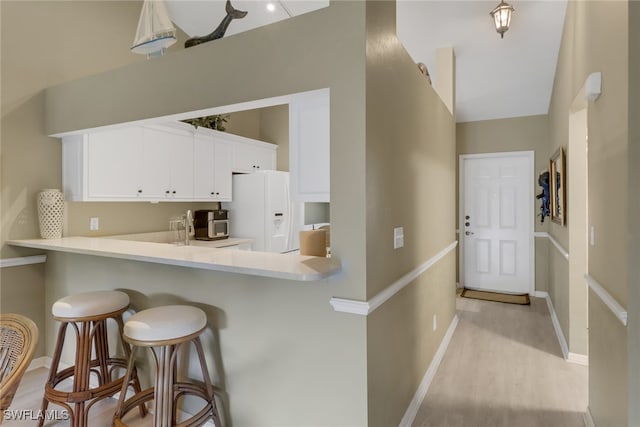 kitchen with white cabinetry, white fridge with ice dispenser, a kitchen breakfast bar, light hardwood / wood-style flooring, and kitchen peninsula