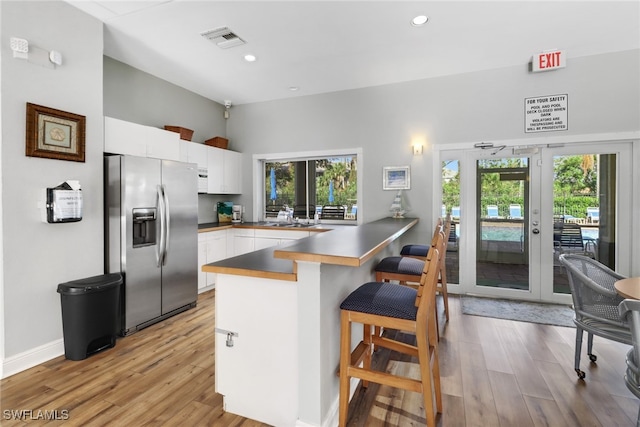 kitchen with kitchen peninsula, stainless steel fridge, light wood-type flooring, a kitchen breakfast bar, and white cabinetry