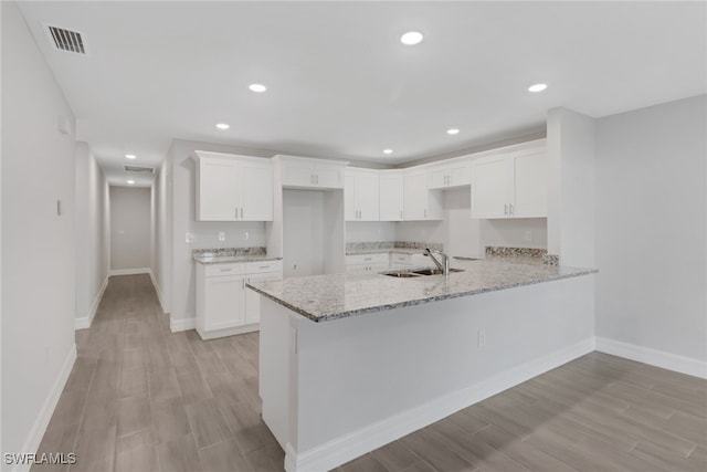 kitchen with white cabinetry, sink, light stone counters, and light wood-type flooring