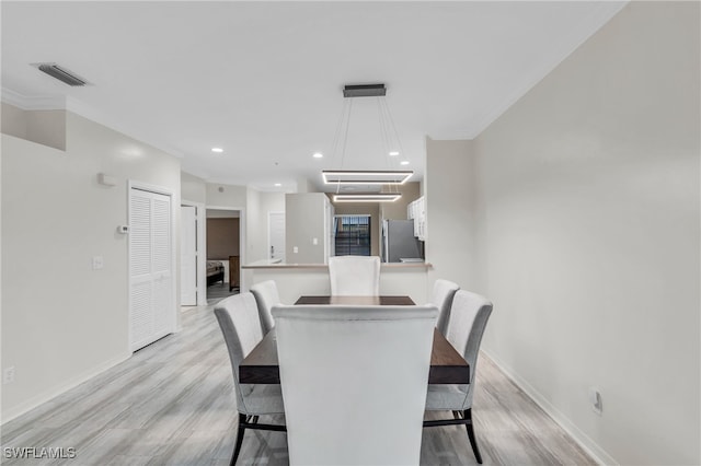 dining area with light hardwood / wood-style floors, an inviting chandelier, and ornamental molding