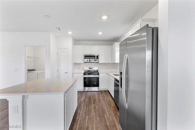 kitchen with appliances with stainless steel finishes, a kitchen island, dark wood-type flooring, washing machine and dryer, and white cabinetry