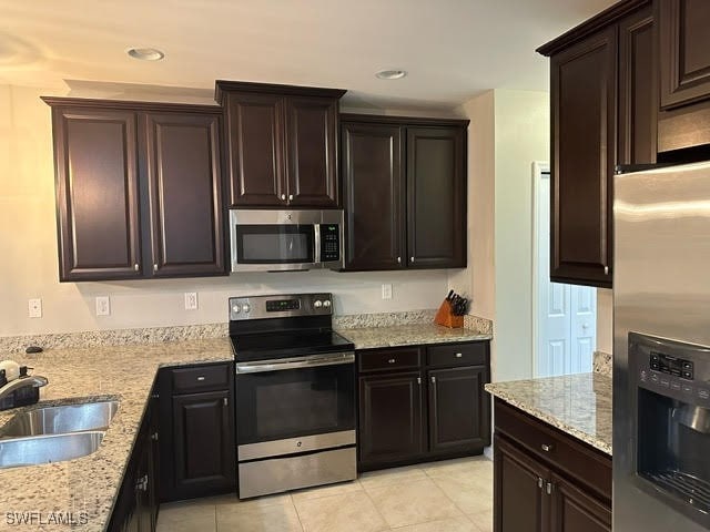 kitchen with appliances with stainless steel finishes, dark brown cabinetry, light tile patterned floors, light stone countertops, and sink