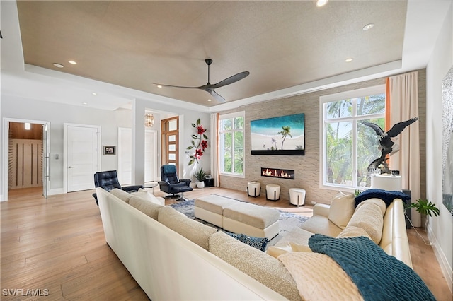 living room featuring a fireplace, a tray ceiling, light hardwood / wood-style flooring, and ceiling fan