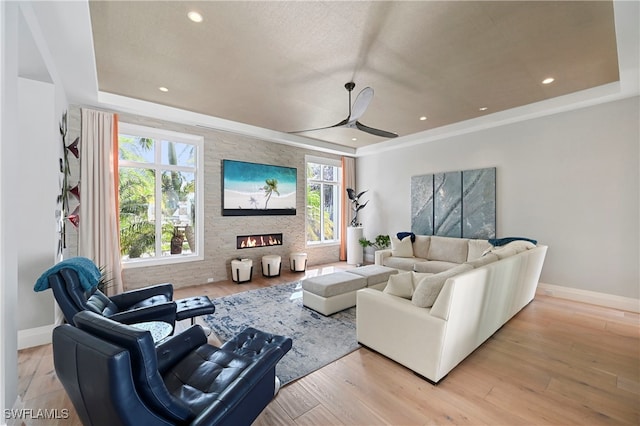 living room with a stone fireplace, ceiling fan, and light hardwood / wood-style flooring