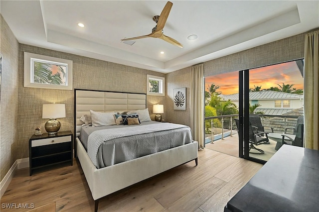 bedroom with a tray ceiling, hardwood / wood-style flooring, ceiling fan, and access to outside