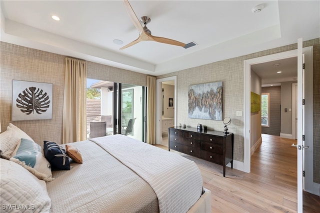 bedroom with access to outside, a raised ceiling, ensuite bath, ceiling fan, and light hardwood / wood-style floors