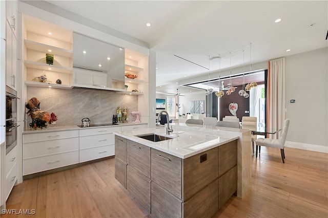 kitchen featuring white cabinetry, sink, black electric stovetop, tasteful backsplash, and a center island with sink