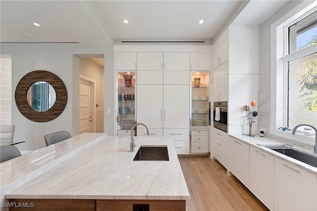 kitchen featuring white cabinetry, sink, oven, and an island with sink