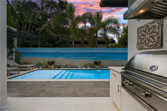 pool at dusk with pool water feature and area for grilling