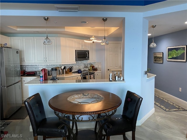 kitchen featuring white cabinets, appliances with stainless steel finishes, decorative light fixtures, and a tray ceiling