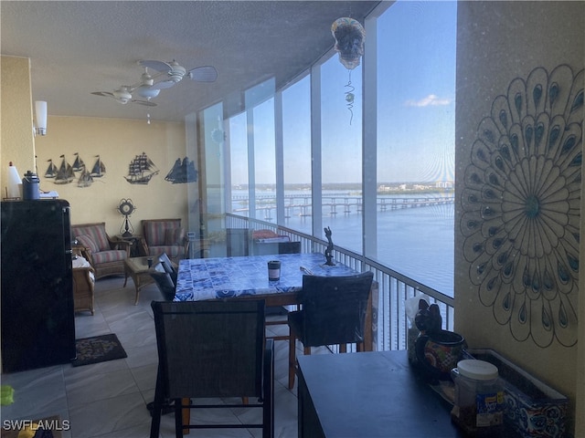 dining room featuring a water view, a textured ceiling, and ceiling fan