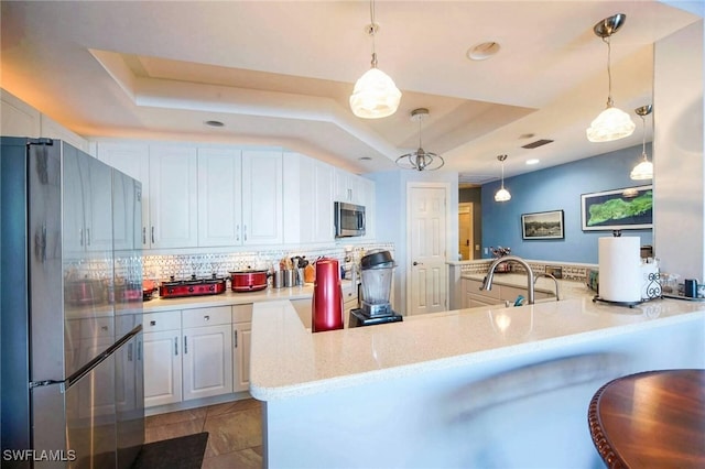 kitchen featuring white cabinetry, stainless steel appliances, a tray ceiling, and kitchen peninsula