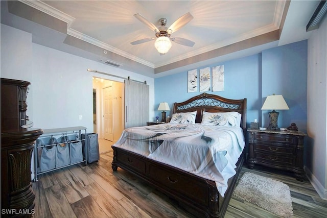 bedroom with ornamental molding, a tray ceiling, ceiling fan, a barn door, and hardwood / wood-style floors