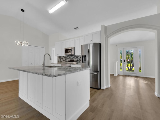 kitchen with stone counters, appliances with stainless steel finishes, vaulted ceiling, white cabinets, and a center island with sink