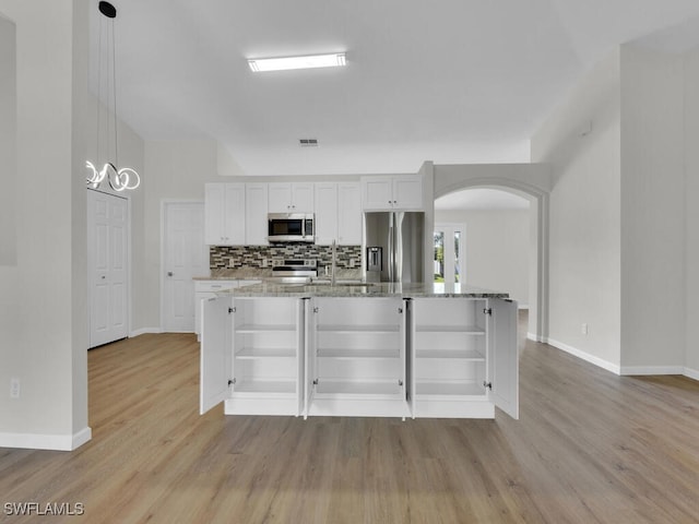 kitchen with hanging light fixtures, appliances with stainless steel finishes, white cabinetry, light stone countertops, and light hardwood / wood-style floors