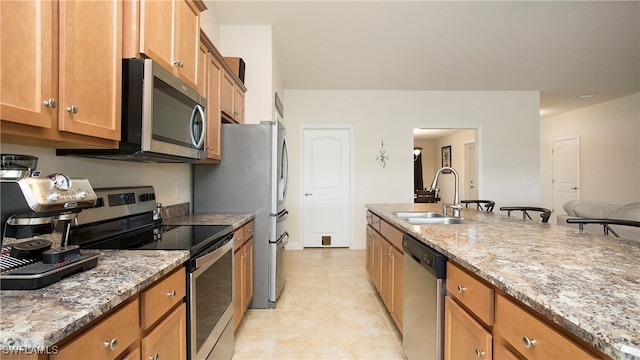 kitchen featuring a kitchen bar, sink, light stone countertops, and stainless steel appliances