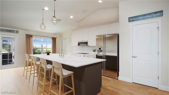 kitchen with lofted ceiling, white cabinets, hanging light fixtures, an island with sink, and appliances with stainless steel finishes