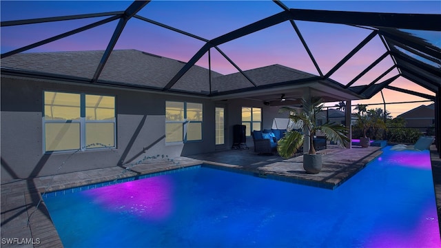 pool at dusk with ceiling fan, a patio, and glass enclosure