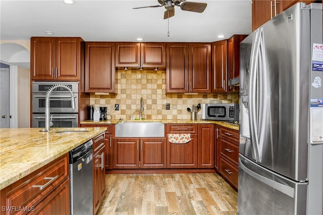 kitchen with light stone counters, sink, light hardwood / wood-style flooring, stainless steel appliances, and backsplash