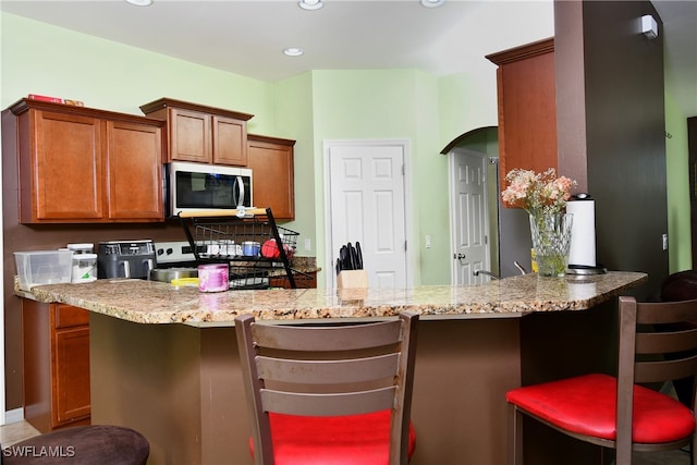 kitchen featuring a kitchen breakfast bar, kitchen peninsula, and light stone counters