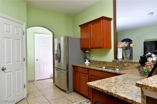 kitchen with stainless steel fridge with ice dispenser, sink, kitchen peninsula, light tile patterned floors, and light stone countertops