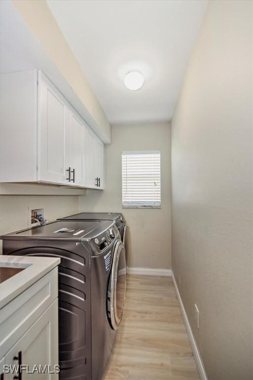 clothes washing area featuring cabinets, washer and dryer, and light wood-type flooring