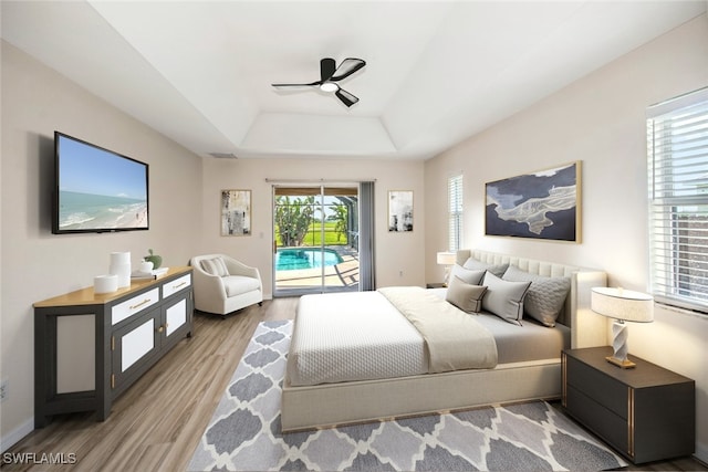 bedroom with ceiling fan, light hardwood / wood-style floors, access to exterior, and a tray ceiling