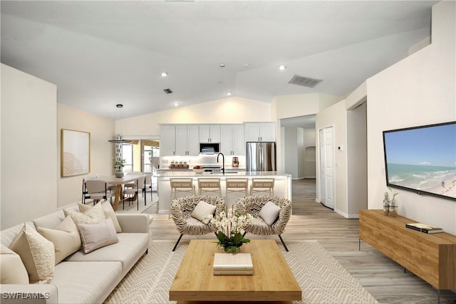 living room featuring sink, light hardwood / wood-style floors, and lofted ceiling