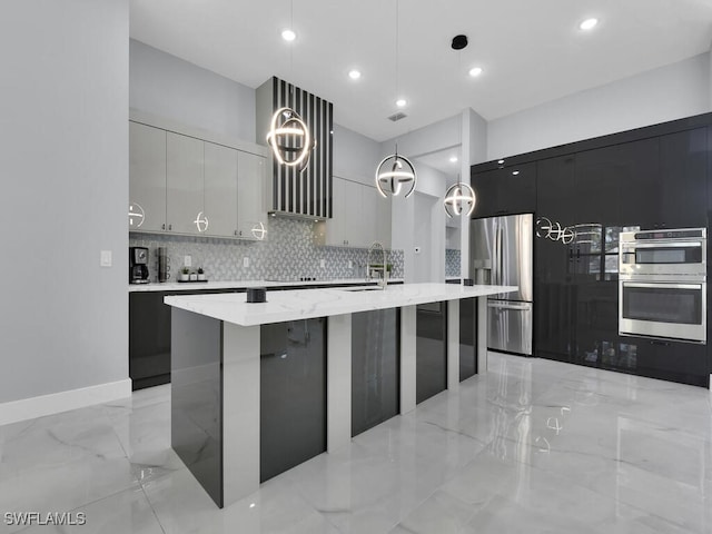 kitchen featuring light stone countertops, an island with sink, stainless steel appliances, pendant lighting, and decorative backsplash