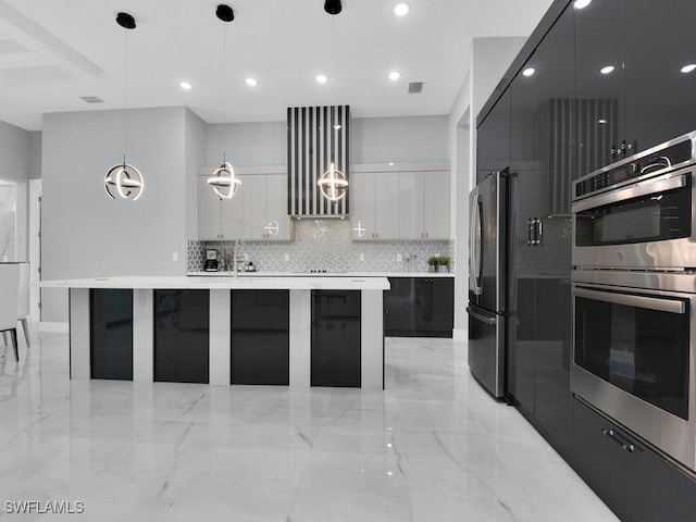 kitchen featuring a large island with sink, hanging light fixtures, stainless steel appliances, white cabinets, and tasteful backsplash