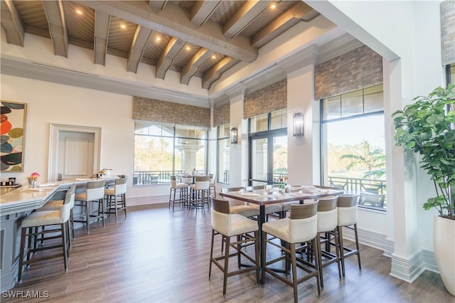 dining space featuring a high ceiling, dark wood-type flooring, and beamed ceiling