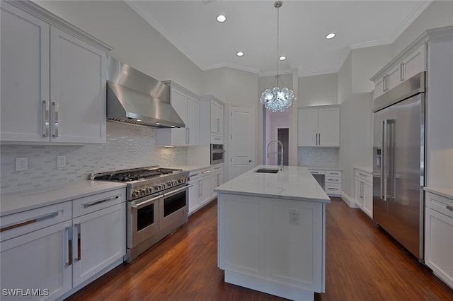 kitchen with wall chimney range hood, premium appliances, a center island with sink, and white cabinets