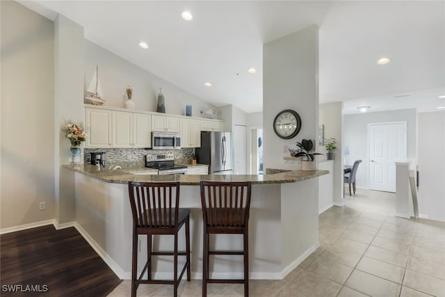 kitchen featuring lofted ceiling, kitchen peninsula, a kitchen bar, appliances with stainless steel finishes, and light stone counters