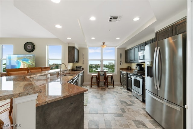 kitchen featuring kitchen peninsula, light stone counters, a kitchen bar, sink, and stainless steel appliances