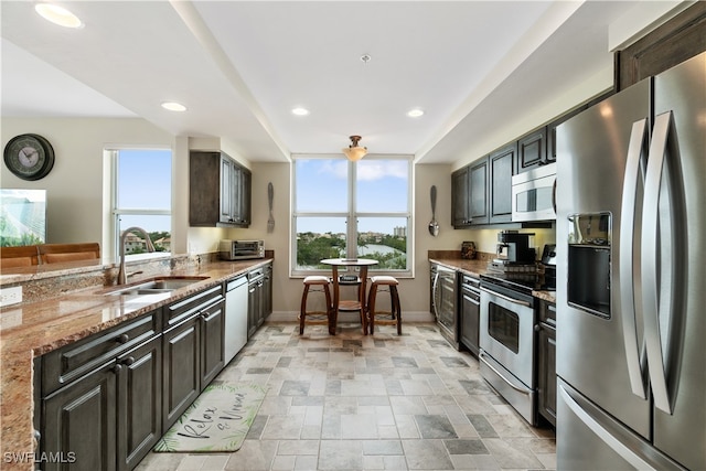 kitchen with a wealth of natural light, sink, appliances with stainless steel finishes, and light stone countertops