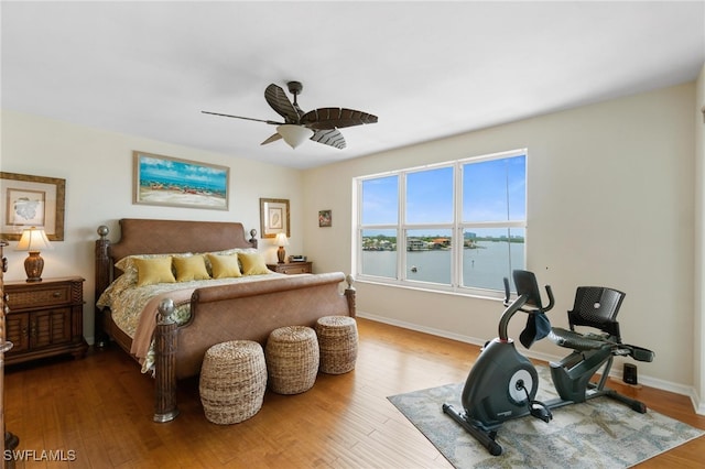 bedroom featuring hardwood / wood-style flooring, a water view, and ceiling fan