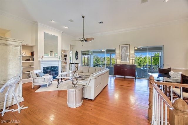 living room with light wood-type flooring, crown molding, a high end fireplace, and ceiling fan