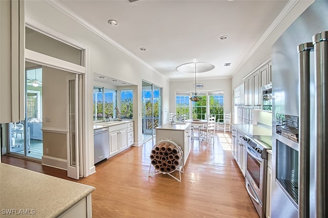 kitchen with white cabinets, ornamental molding, a kitchen island, light hardwood / wood-style flooring, and stainless steel appliances