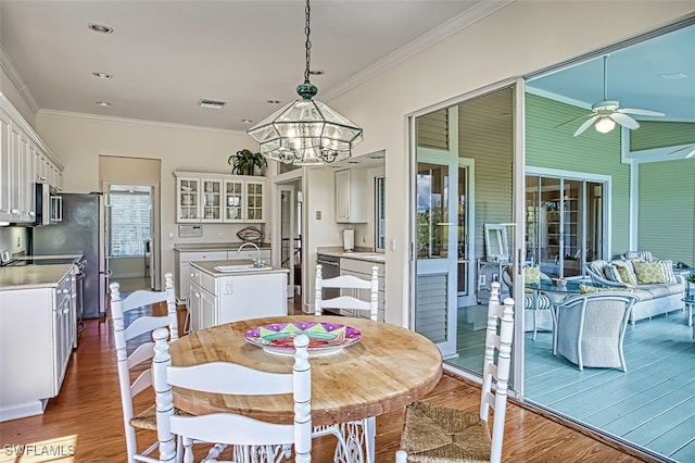 dining space with ceiling fan with notable chandelier, sink, hardwood / wood-style floors, and crown molding