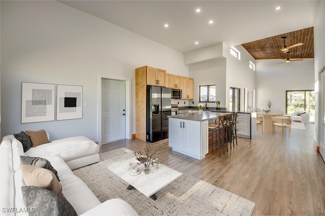 living room with a high ceiling, light wood-type flooring, ceiling fan, and wood ceiling