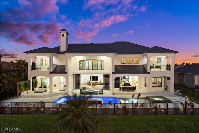 back house at dusk with a patio, a balcony, an outdoor hangout area, and a pool with hot tub