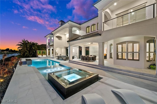 pool at dusk with an in ground hot tub and a patio area