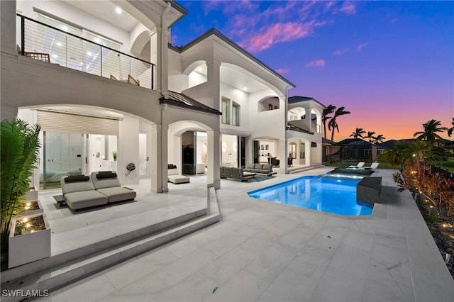 pool at dusk with a patio, outdoor lounge area, and an in ground hot tub