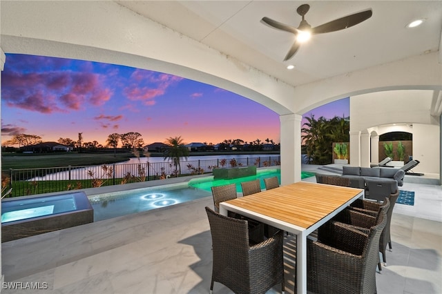 pool at dusk featuring a water view, an in ground hot tub, ceiling fan, an outdoor hangout area, and a patio