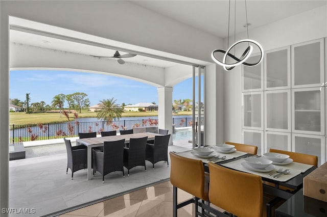 tiled dining area featuring a water view and ceiling fan with notable chandelier