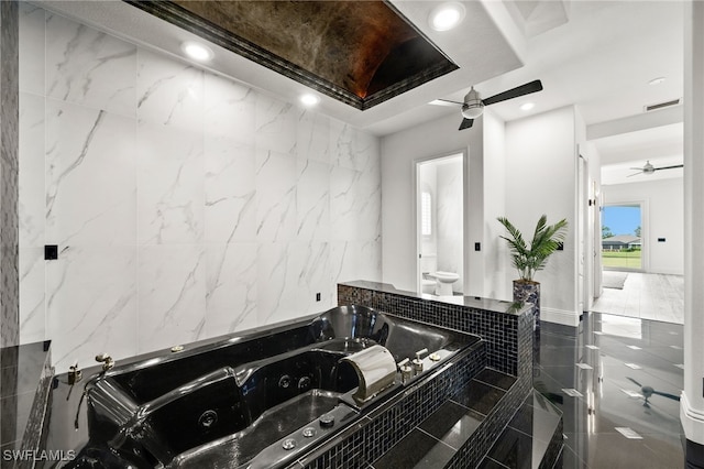 bathroom with a relaxing tiled tub, ceiling fan, and toilet