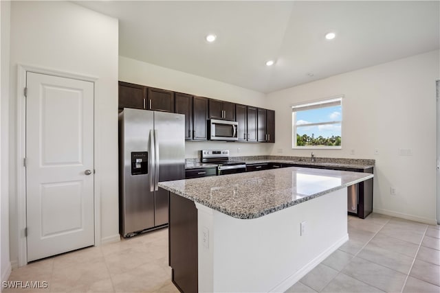 kitchen with light stone counters, light tile patterned flooring, a kitchen island, stainless steel appliances, and dark brown cabinetry