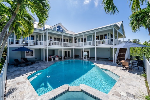 rear view of house with a patio, a balcony, and a swimming pool with hot tub